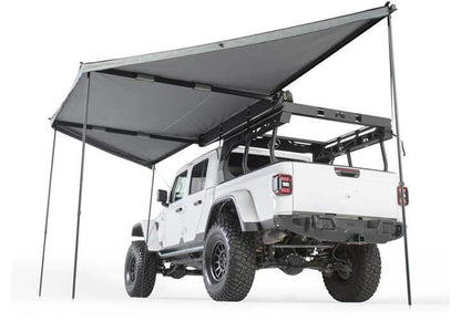 Smittybilt 180° awning providing shade over a white off-road vehicle with a roof rack.